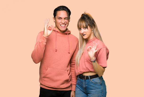 ピンクの背景の上に指でOKサインを示す若いカップル - 写真・画像