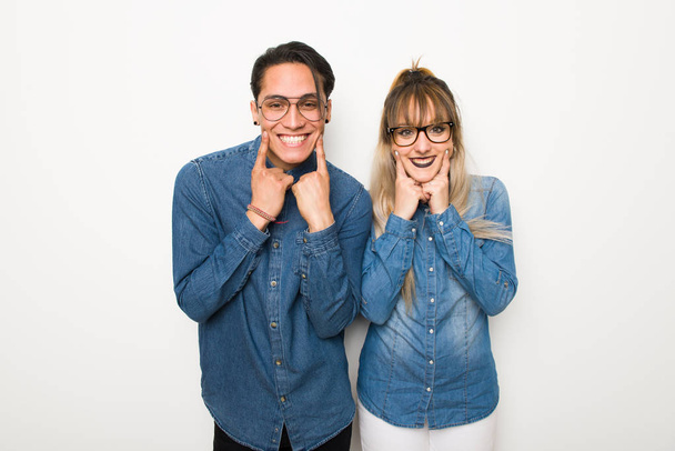 Νεαρό ζευγάρι με γυαλιά χαμογελώντας με μια χαρούμενη και ευχάριστη έκφραση - Φωτογραφία, εικόνα
