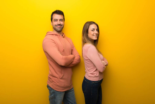 Group of two people on yellow background keeping the arms crossed in lateral position while smiling - Photo, Image