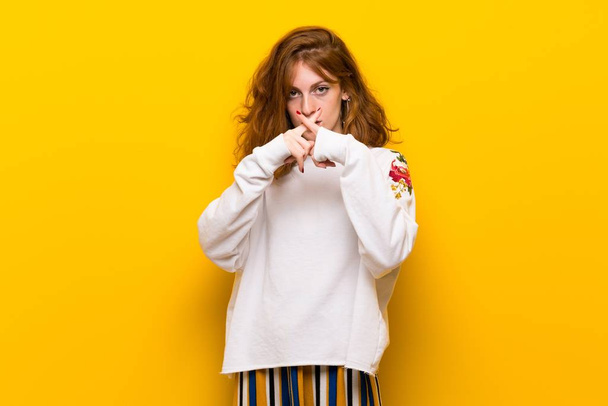 Young redhead woman over yellow wall showing a sign of silence gesture - Fotoğraf, Görsel