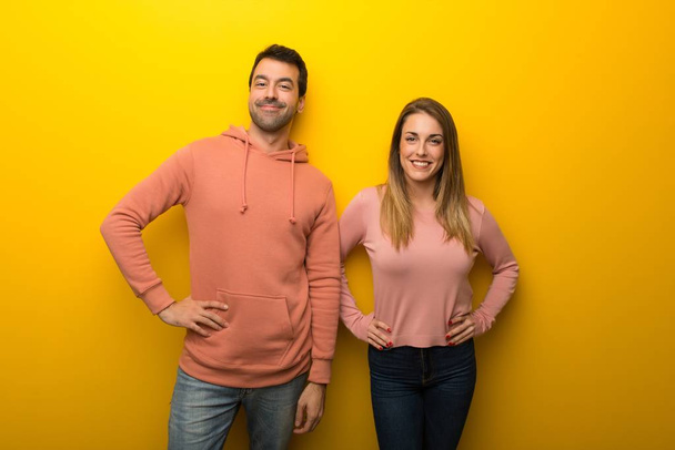 Group of two people on yellow background posing with arms at hip and laughing looking to the front - Fotó, kép