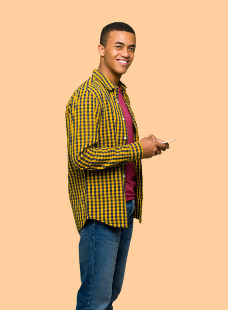 junger afroamerikanischer Mann sendet eine Nachricht mit dem Handy auf isoliertem Hintergrund - Foto, Bild