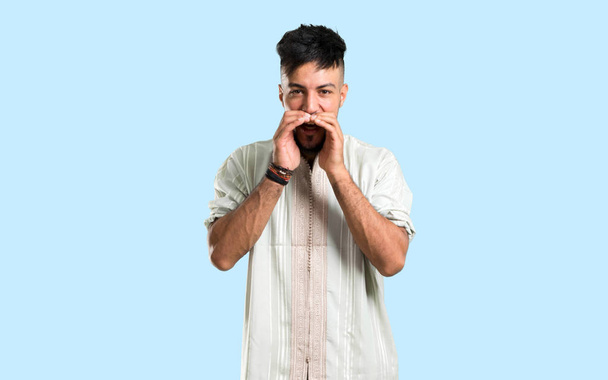 Arab fiatalember visel tipikus arab ruhák kiabáló száj széles nyitott kék háttér - Fotó, kép