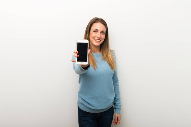 Mujer rubia sobre fondo blanco aislado mostrando el móvil
 - Foto, imagen