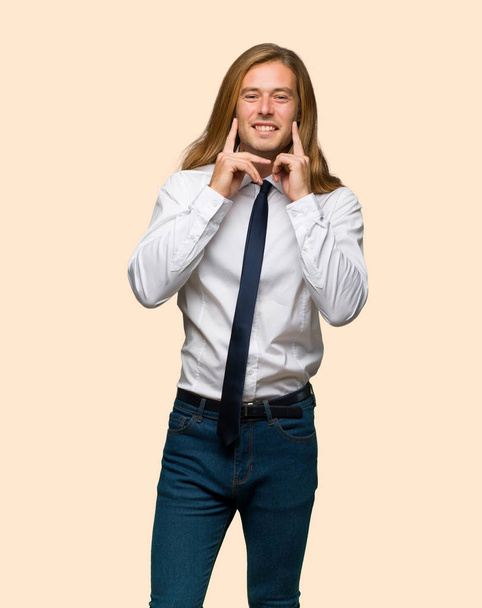 Blonder Geschäftsmann mit langen Haaren lächelt mit einem fröhlichen und angenehmen Gesichtsausdruck auf isoliertem Hintergrund - Foto, Bild