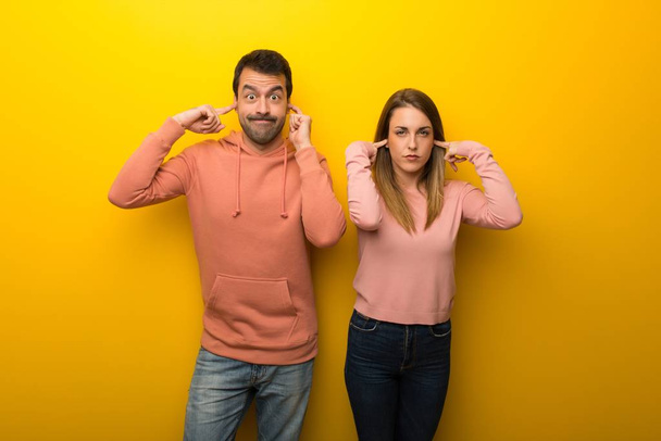 Group of two people on yellow background covering both ears with hands - Photo, Image