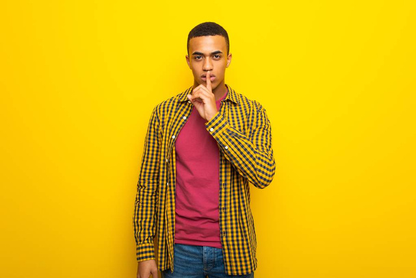 Jeune homme afro-américain sur fond jaune montrant un signe de silence geste mettant le doigt dans la bouche
 - Photo, image