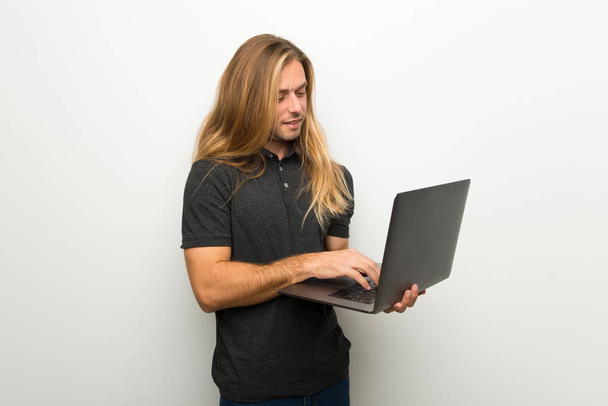 Blond man with long hair over white wall with laptop - Foto, Imagem