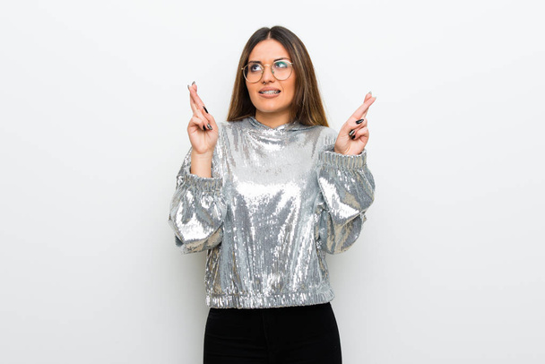 Young woman with glasses over white wall with fingers crossing and wishing the best - Foto, afbeelding