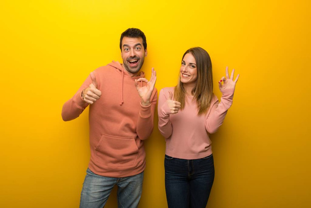 Group of two people on yellow background showing ok sign with and giving a thumb up gesture - Photo, Image