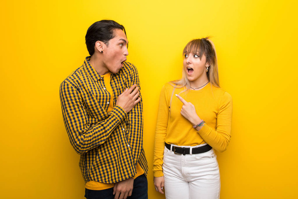 Young couple over vibrant yellow background surprised and pointing side - Photo, Image