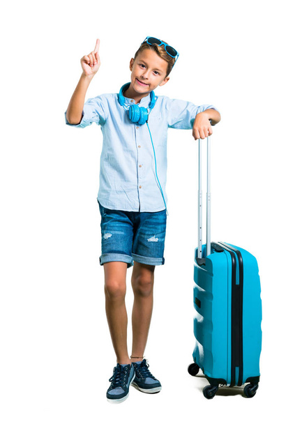 Çocuk tam vücut güneş gözlüğü ve kulaklık bavulunu izole beyaz zemin üzerinde bir numara işareti sayma ile seyahat ile - Fotoğraf, Görsel