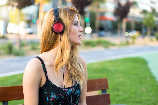 Досить молода дівчина-підліток в парку слухає музику з навушниками
 - Фото, зображення