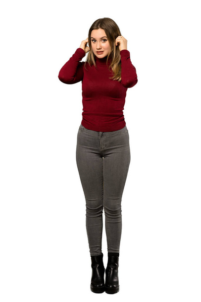 A full-length shot of a Teenager girl with turtleneck frustrated and covering ears with hands over isolated white background - Photo, image