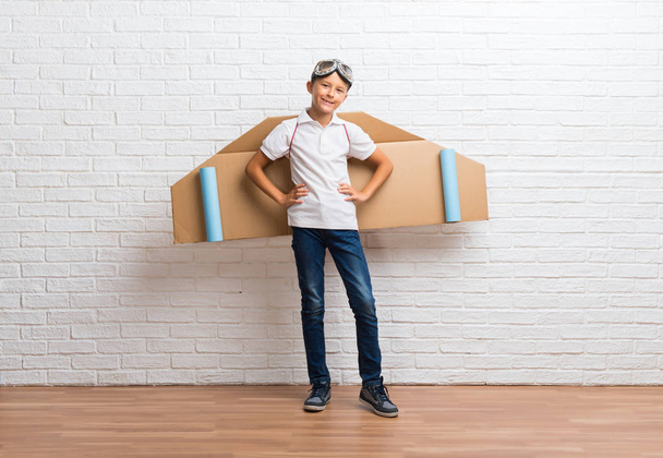Garçon jouer avec des ailes d'avion en carton sur son dos posant avec les bras à la hanche
 - Photo, image