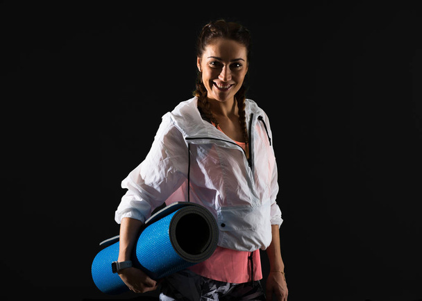 Sportlerin auf dunklem Hintergrund mit Matte - Foto, Bild
