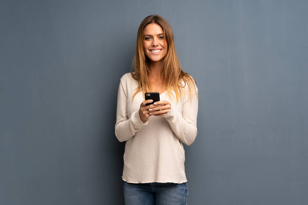 Donna bionda su sfondo grigio invio di un messaggio con il cellulare
 - Foto, immagini