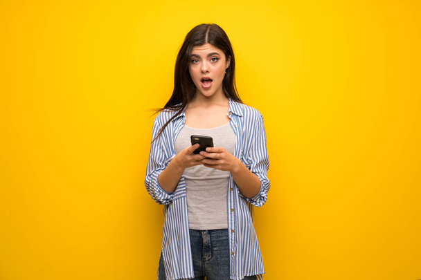 Teenager girl over yellow wall surprised and sending a message - Foto, Imagem