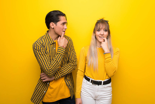 Young couple over vibrant yellow background having doubts while looking up - Photo, Image