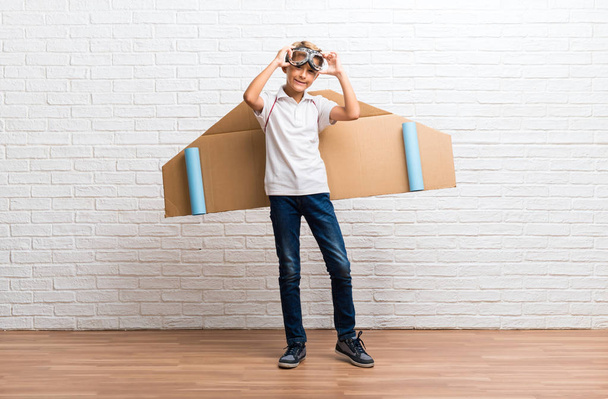 Niño jugando con alas de avión de cartón
 - Foto, Imagen