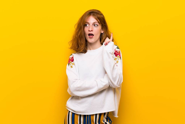Jonge roodharige vrouw over gele muur een idee de vinger omhoog te denken - Foto, afbeelding