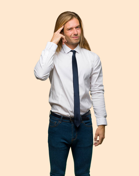 Hombre de negocios rubio de pelo largo haciendo el gesto de locura poniendo el dedo en la cabeza sobre un fondo aislado
 - Foto, Imagen
