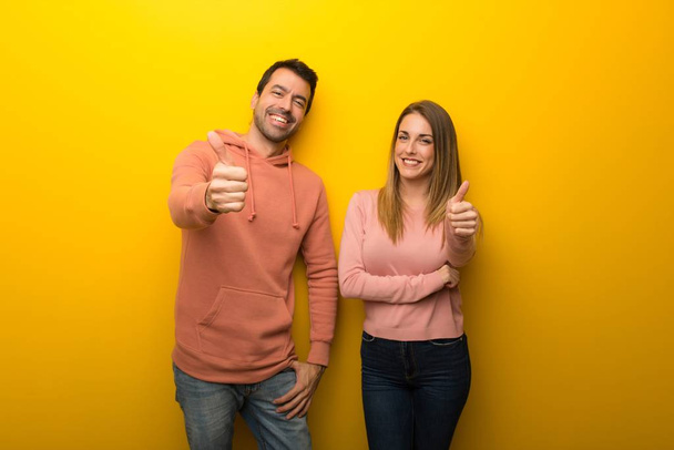 Group of two people on yellow background giving a thumbs up gesture because something good has happened - Photo, Image