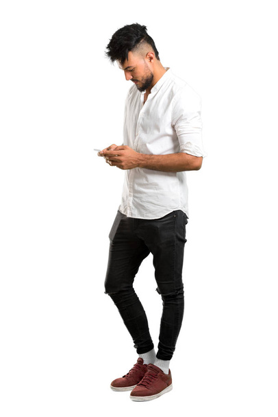 Un plan complet d'un jeune homme arabe avec chemise blanche gardant une conversation avec le téléphone portable avec quelqu'un sur fond blanc isolé
 - Photo, image
