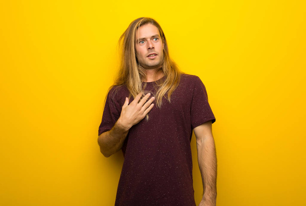 Blond man with long hair over yellow wall surprised and shocked while looking right - Foto, afbeelding