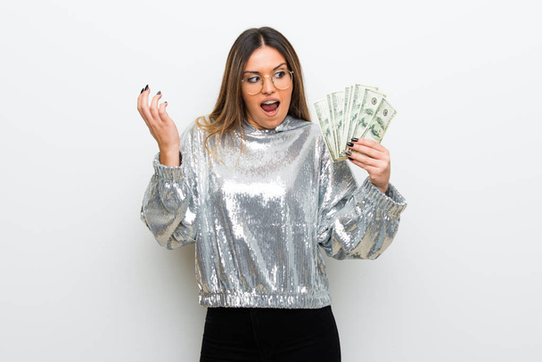 Young woman with glasses over white wall taking a lot of money - Foto, afbeelding