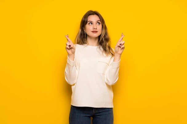 Teenager girl over yellow wall with fingers crossing and wishing the best - Foto, Bild
