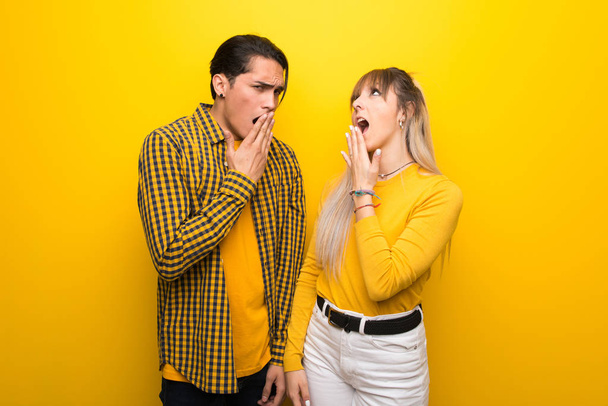 Молодая пара на ярком желтом фоне зевает и закрывает широко раскрытый рот рукой
 - Фото, изображение