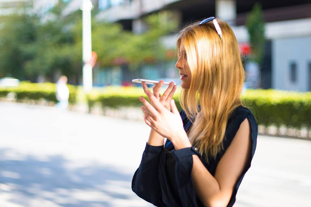 Pretty young teenager girl sending an audio by mobile at the street - Foto, Imagen