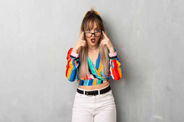 Девушка в разноцветной одежде в очках и удивлена
 - Фото, изображение