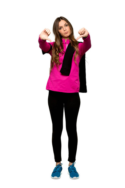 Full-length shot of Young sport woman showing thumb down with both hands over isolated white background - Foto, afbeelding