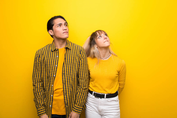 Jovem casal sobre vibrante fundo amarelo olhando para cima com rosto sério
 - Foto, Imagem