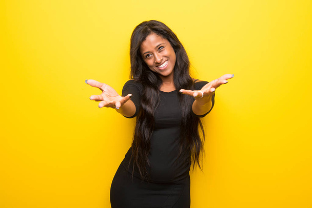 Young afro american woman on vibrant yellow background presenting and inviting to come with hand - Фото, изображение