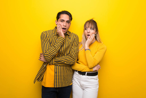 Young couple over vibrant yellow background surprised and shocked while looking right - Photo, Image