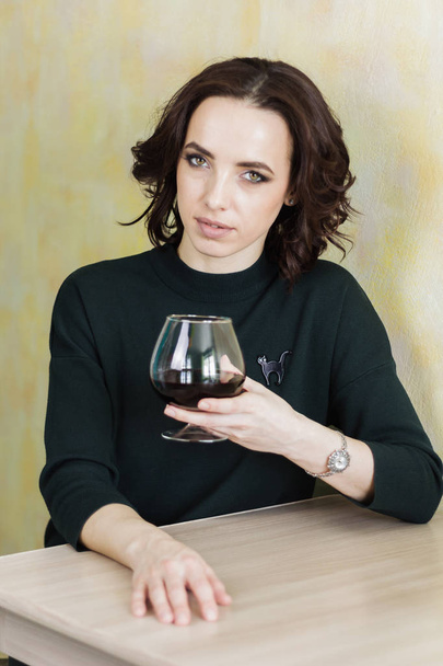 beautiful woman sitting at the table holding a wine glass with red wine and looking at the camera - 写真・画像