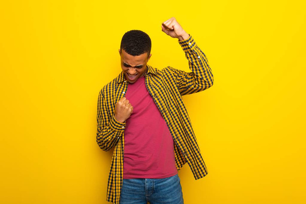 Jeune homme afro-américain sur fond jaune célébrant une victoire
 - Photo, image