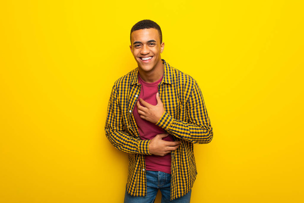 Nuori afro amerikkalainen mies keltaisella taustalla hymyilee paljon, kun taas laittaa kädet rinnassa
 - Valokuva, kuva