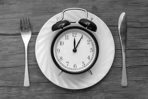 Reloj despertador con tenedor y cuchillo en la mesa. Hora de comer, desayuno, almuerzo y concepto de cena. Concepto blanco y negro
 - Foto, imagen