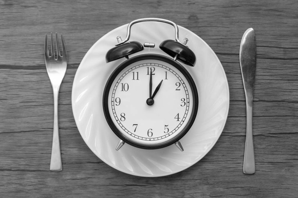 Relógio despertador com garfo e faca na mesa. Hora de comer, Café da manhã, Hora de almoço e jantar conceito. Conceito preto e branco
 - Foto, Imagem