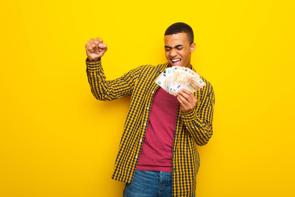 Bir sürü para alarak sarı zemin üzerine genç afro Amerikalı adam - Fotoğraf, Görsel