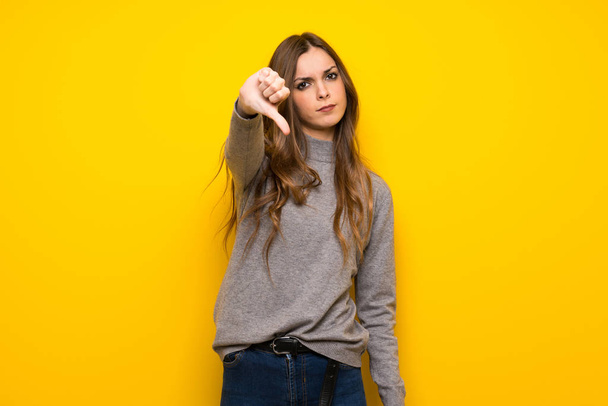 Başparmak aşağı negatif ifade işaretiyle gösterilen sarı duvarın üzerinden genç kadın - Fotoğraf, Görsel