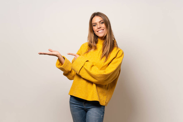 Frau mit gelbem Pullover über isolierter Wand, die imaginären Kopierraum auf der Handfläche hält, um eine Anzeige einzufügen - Foto, Bild