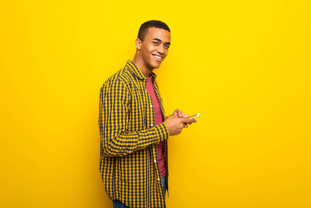 junger afroamerikanischer Mann auf gelbem Hintergrund sendet eine Nachricht mit dem Handy - Foto, Bild