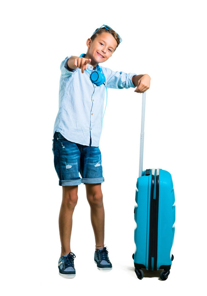Całe ciało dziecka z okulary i słuchawki podróży wraz z walizką wskazuje palcem na Ciebie na na białym tle - Zdjęcie, obraz