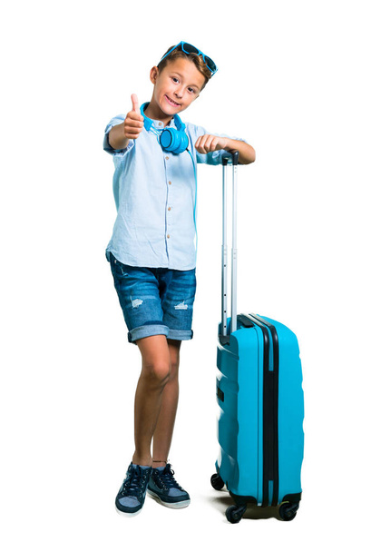 Повне тіло дитини з сонцезахисними окулярами та навушниками, які подорожують з валізою, даючи великий жест і посміхаючись на ізольованому білому тлі
 - Фото, зображення