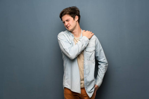 Hombre adolescente con chaqueta de jean sobre pared gris sufriendo de dolor en el hombro por haber hecho un esfuerzo
 - Foto, Imagen